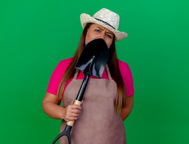 Middle aged gardener woman in apron and hat holding shovel