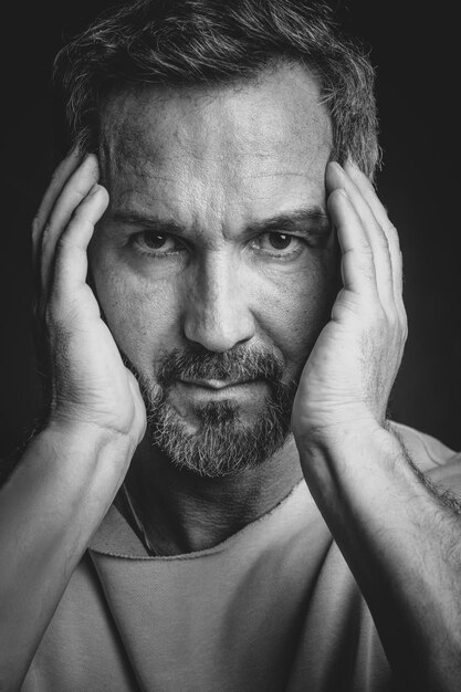 Middle aged grey haired man hold his face with hands looking at camera Handsome middle aged man in black and white photo Black and white portrait of attractive beautiful serious man