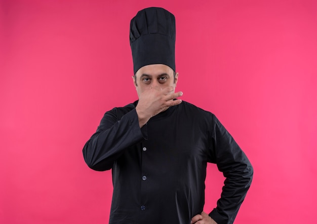 Free photo middle-aged male cook in chef uniform closed nose on isolated pink wall