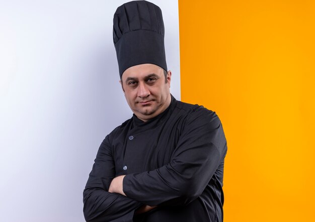 middle-aged male cook in chef uniform crossing hands with withe wall on yellow wall with copy space