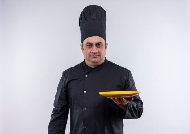 middle-aged male cook in chef uniform holding plate on isolated white wall