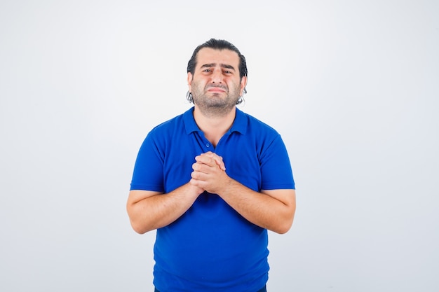 Uomo di mezza età in maglietta blu che mostra le mani giunte in gesto di supplica