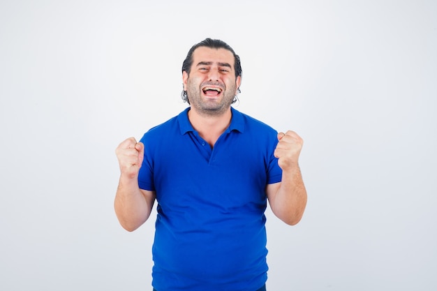 Middle aged man in blue t-shirt showing winner gesture and looking lucky