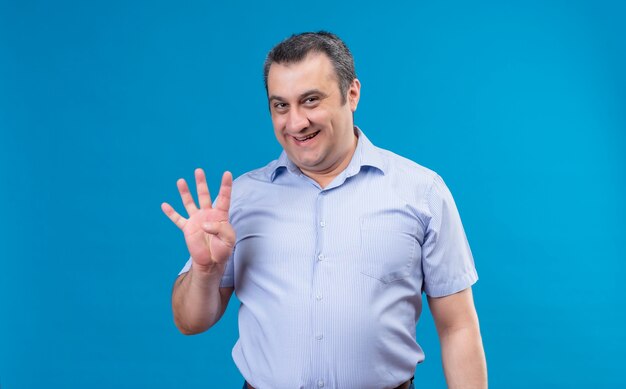 Middle-aged man in blue vertical striped shirt with happy face showing and pointing up with finger number four on a blue background