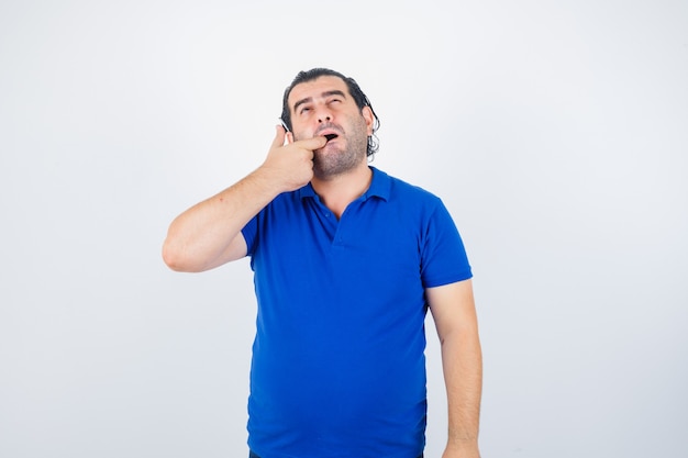 Middle aged man checking his teeth  in polo t-shirt and looking cheerless. front view.