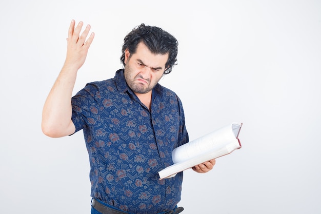 Uomo di mezza età che tiene il libro mentre si alza la mano in camicia e sembra arrabbiato, vista frontale.