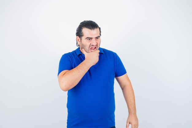 Middle aged man holding hand on chin in blue t-shirt and looking angry