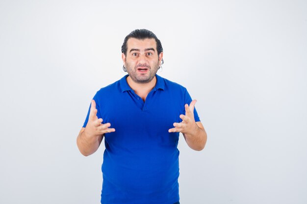 Мужчина средних лет в синей футболке агрессивно держит руки за руки и выглядит озадаченным. передний план.