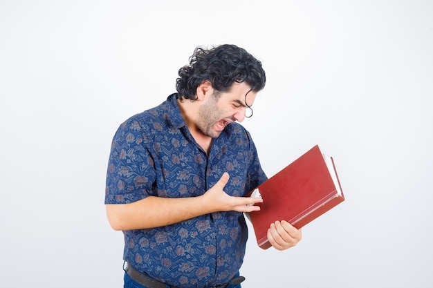 Middle aged man looking at book in shirt and looking furious. front view.