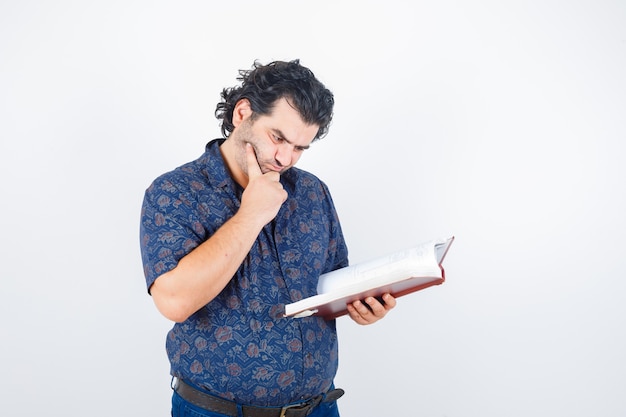 Middle aged man looking at book in shirt and looking pensive. front view.