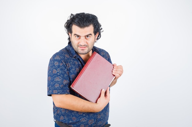 Middle aged man looking at camera while holding book in shirt and looking confident. front view.