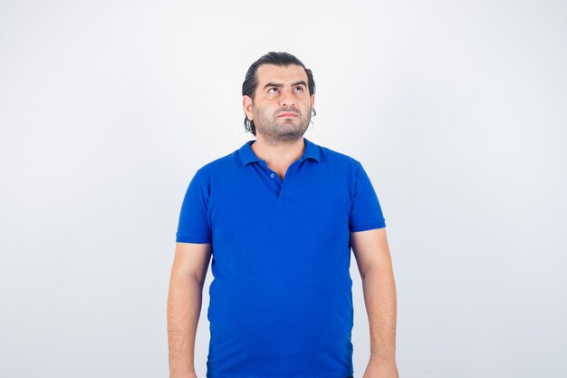 Middle aged man looking up in blue t-shirt and looking thoughtful