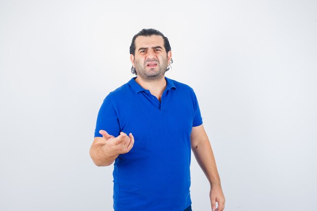 Middle aged man pointing at front in blue t-shirt and looking puzzled