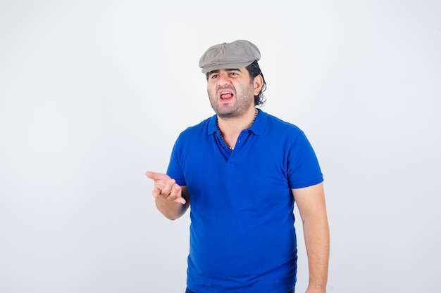 Мужчина средних лет в футболке-поло, в шляпе из плюща указывает и выглядит агрессивно