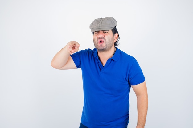 Middle aged man in polo t-shirt, ivy hat showing V sign and looking aggressive , front view.