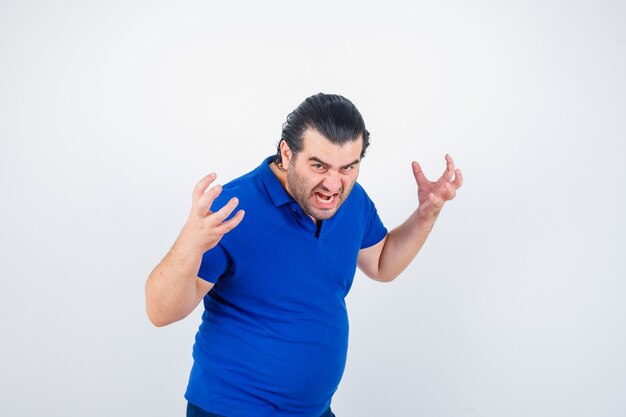 Middle aged man in polo t-shirt keeping hands in aggressive manner and looking angry