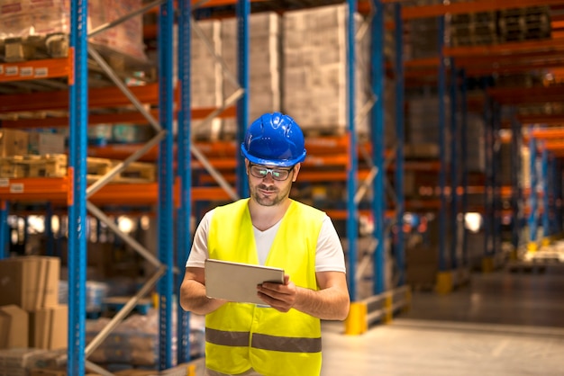 Middle aged man in protective work wear working on a tablet in large warehouse storage center