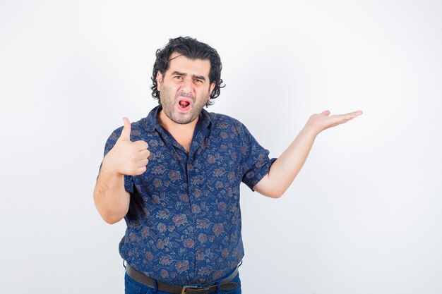 Middle aged man in shirt holding something while showing thumb up and looking pleased , front view.