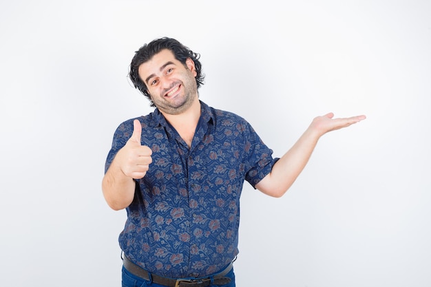 Middle aged man in shirt holding something while showing thumb up and looking pleased , front view.