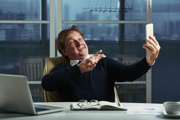 Middle aged man taking selfies at his office desk