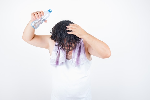 Middle aged man in tank top, towel pouring water on the head with bottle and looking funny , front view.