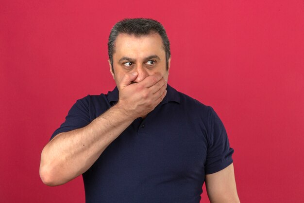 Middle aged man wearing polo shirt covering mouth with hand scared keeping secret information over isolated pink wall