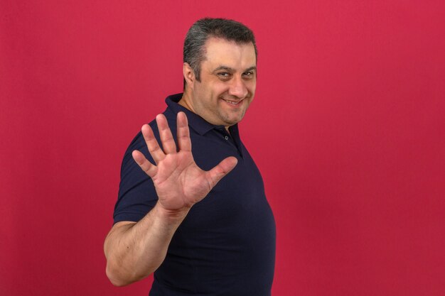 Middle aged man wearing polo shirt with smile on face and showing number five with fingers over isolated pink wall