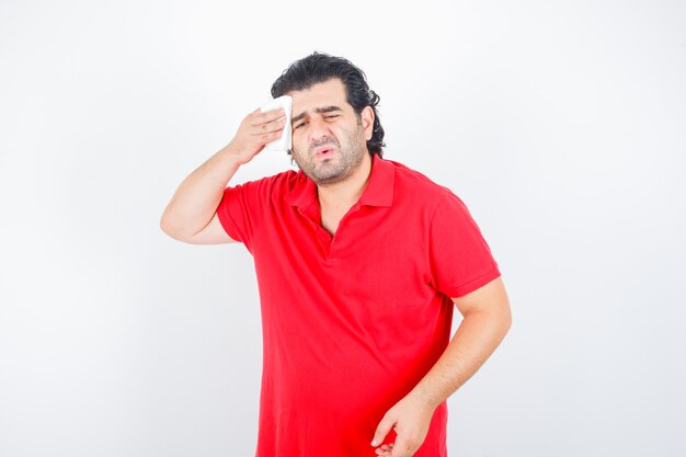 Middle aged man wiping sweat in red t-shirt and looking sick. front view.