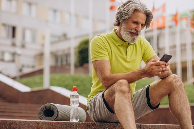 Middle aged sportsman sitting on stairs using phone