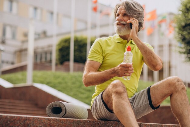 Middle aged sportsman sitting on stairs using phone