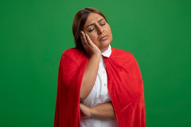 Middle-aged superhero female with closed eyes showing sleep gesture isolated on green background