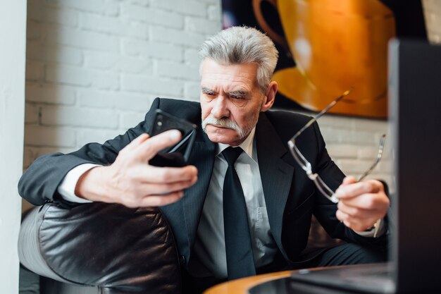 Несчастный бизнесмен средних лет в современном ресторане с помощью ноутбука и телефона.