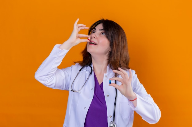 흰색 코트를 입고 청진기와 오렌지 배경 위에 서있는 알약을 복용하려고 손에 약을 들고 중간 세 여자 의사