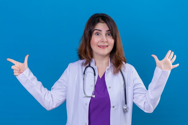 Middle aged woman doctor wearing white coat and with stethoscope showing and pointing up with fingers number seven while smiling confident and happy standing over blue background