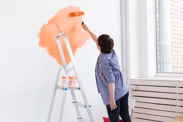Женщина средних лет красит стены нового дома. ремонт, ремонт и концепция косметического ремонта.