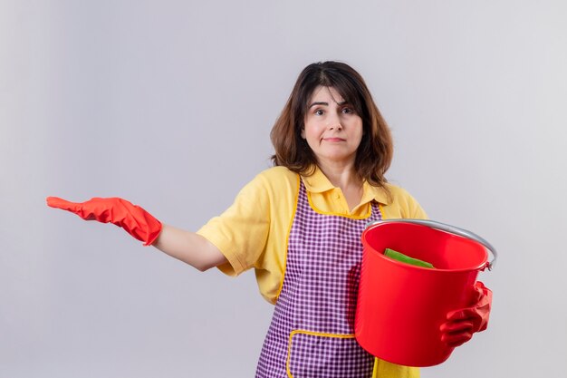 Middle aged woman wearing apron and rubber gloves holding bucket with cleaning tools