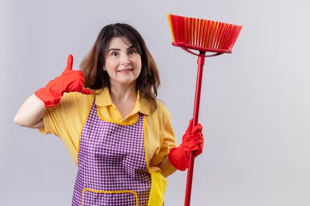 Middle aged woman wearing apron and rubber gloves standing with mop making call me gesture