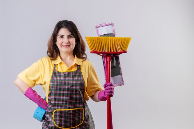 Middle aged woman wearing apron and rubber gloves standing with mop