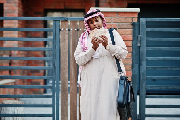 中東のアラブのビジネスマンは、黒いハンドバッグとユーロのお金でモダンな建物に対して通りにポーズをとった