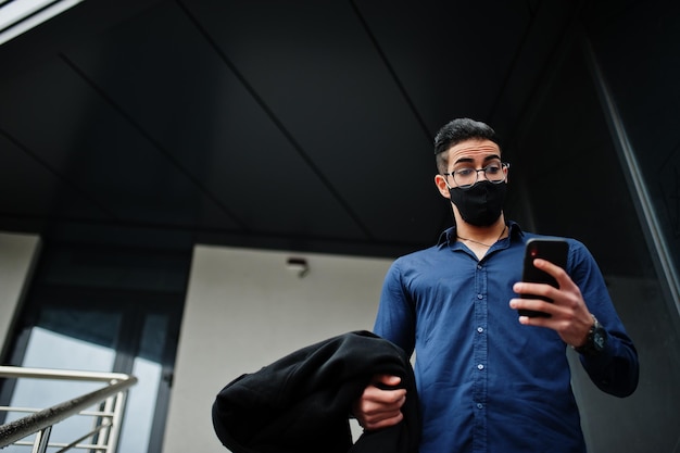 Middle eastern entrepreneur wear black face mask and eyeglasses look at mobile phone New normal life after coronavirus pandemia