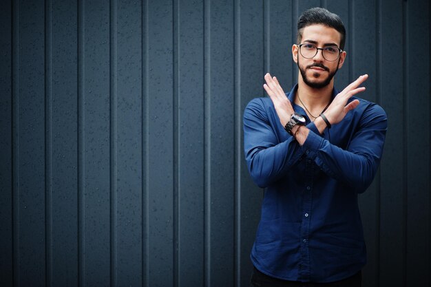 Ближневосточный предприниматель носит очки в синей рубашке на фоне стальной стены и запрещающий знак