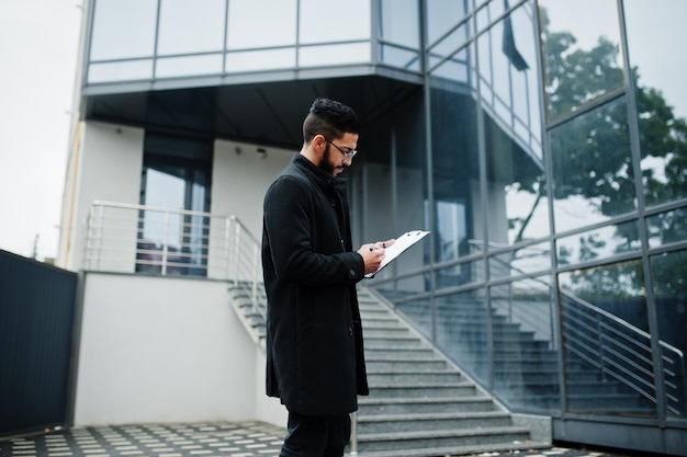 Middle eastern man wear black coat eyeglasses writing contract on clipboard