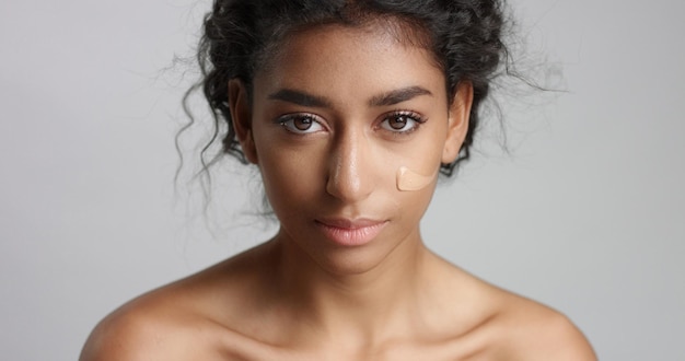 Ближневосточная молодая женщина в студии с тональным кремом на щеке крупным планом Прикосновение к коже
