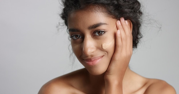 Middle eastern young woman in studio with a foundation on cheek closeup Touching skin