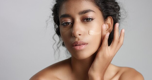Middle eastern young woman in studio with a foundation on cheek closeup Touching skin