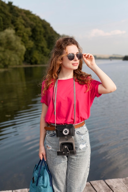 Middle shot woman with camera posing in front of lake