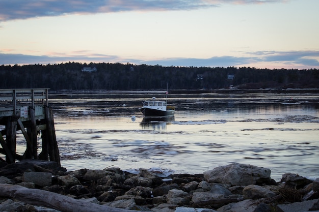 Middle size fishing boat cruising by the shore in the sea close to a rocky beach before dusk