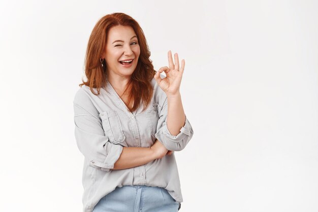 Middleaged redhead elegant stylish mother assuring everything okay count me show ok excellent gesture winking assertive confident give positive opinion standing satisfied approval white background