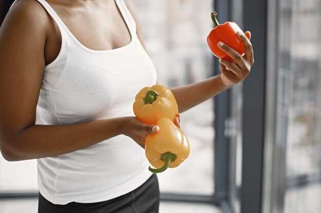 Midsection of black young woman in studio holding a yellow and red pepper