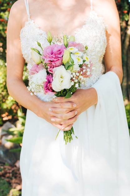 Midsection of a bride in white dress holding flower bouquet in her hands